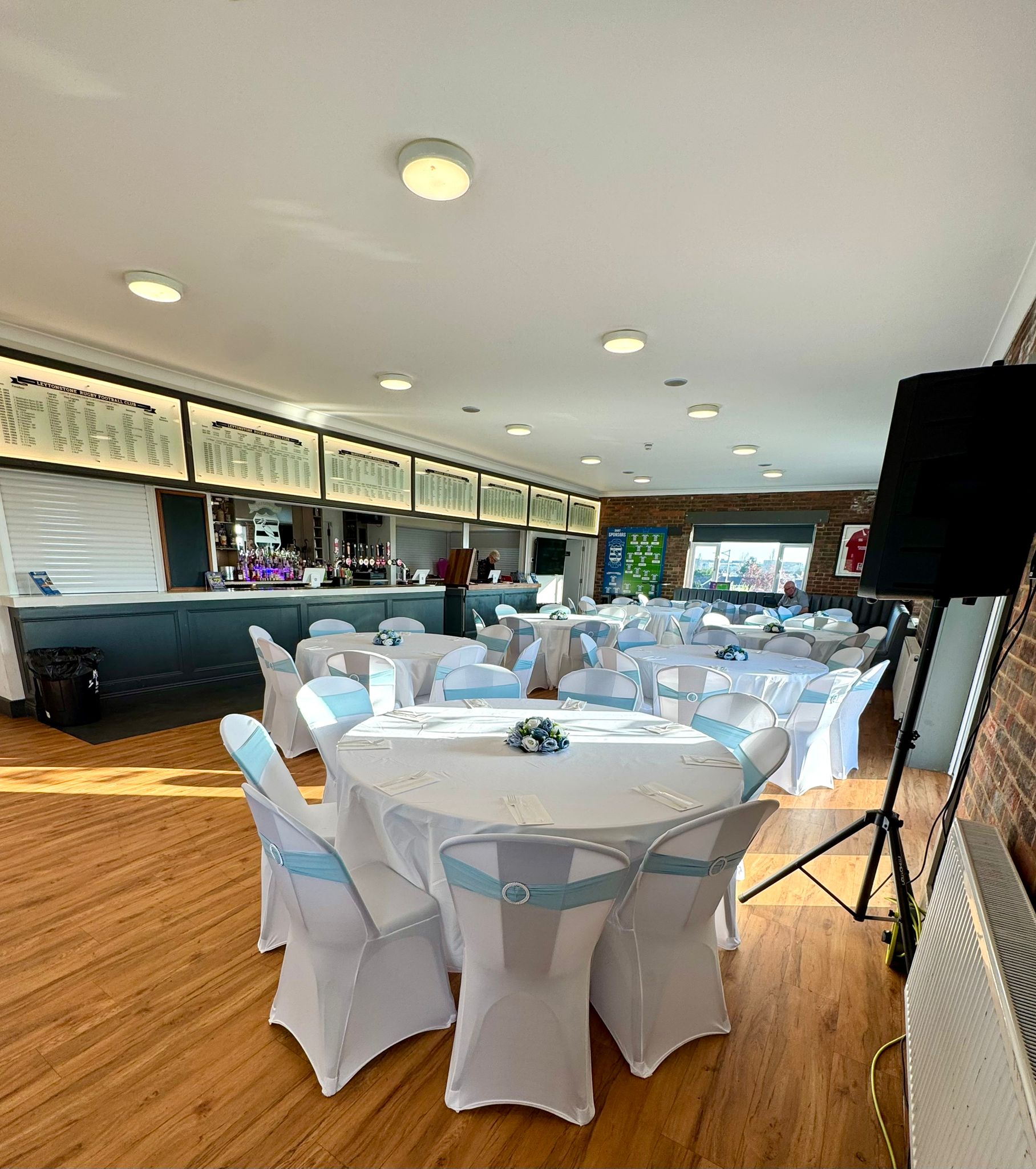 The Centenary Field function room featuring a professional bar and round tables decorated for a wedding